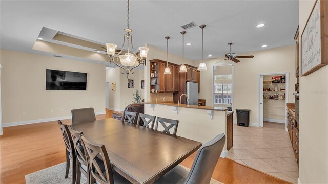 dining space with sink, a raised ceiling, ceiling fan, and light wood-type flooring