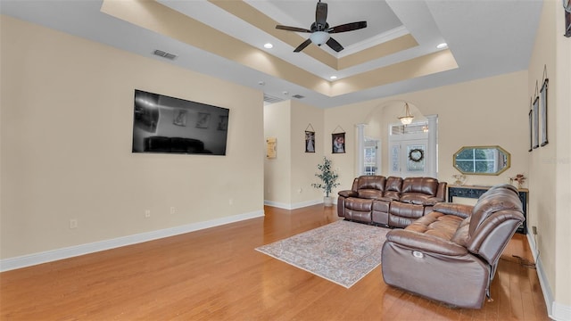 living room with hardwood / wood-style flooring, ceiling fan, and a raised ceiling