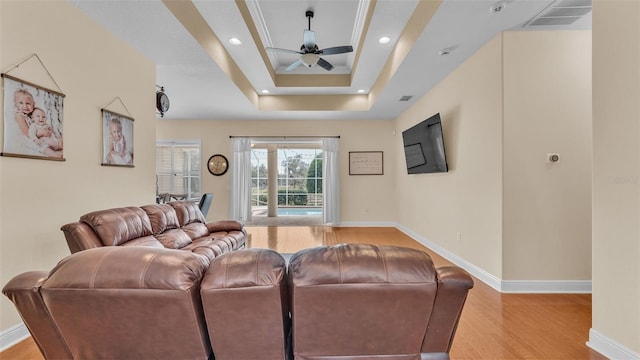 living room with ceiling fan, a raised ceiling, and light wood-type flooring