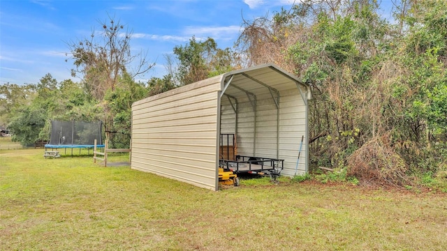 view of outdoor structure with a trampoline, a yard, and a carport