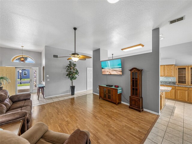 living room featuring baseboards, visible vents, a textured ceiling, and light wood finished floors