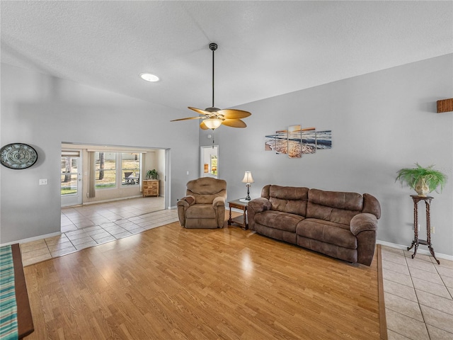 living room featuring a ceiling fan, light wood-type flooring, a textured ceiling, and baseboards