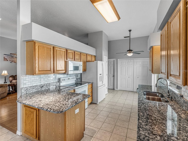 kitchen featuring a peninsula, white appliances, a sink, dark stone counters, and tasteful backsplash