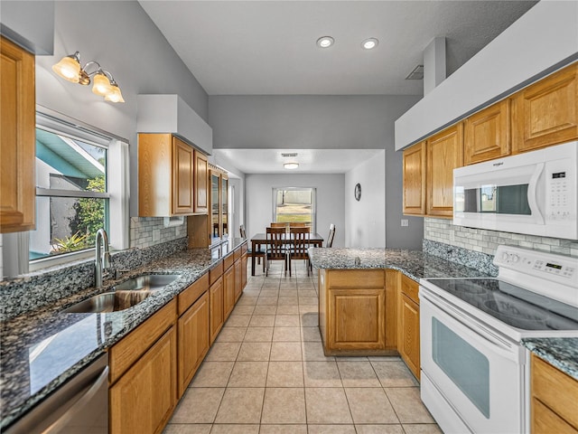 kitchen featuring light tile patterned floors, tasteful backsplash, a sink, white appliances, and a peninsula