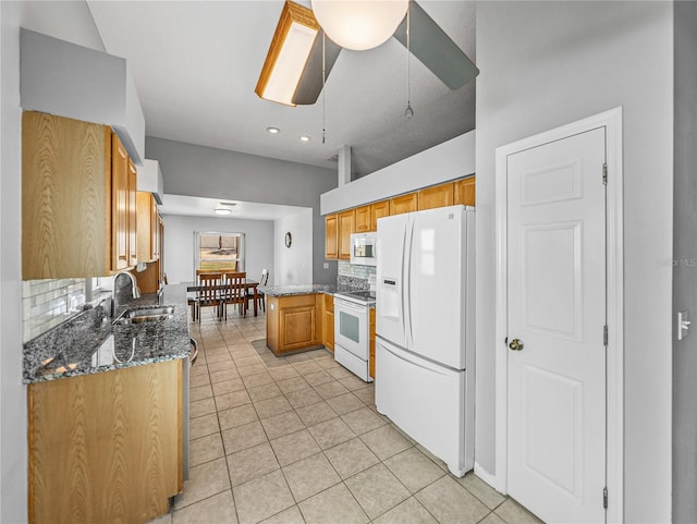 kitchen featuring light tile patterned floors, white appliances, a sink, backsplash, and dark stone countertops