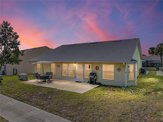 back of house at dusk featuring a yard, stucco siding, a patio, and central AC unit