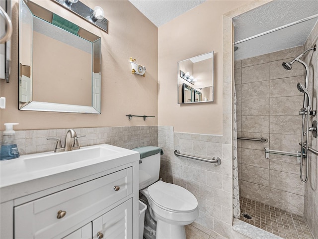 full bathroom with a wainscoted wall, tile walls, toilet, a tile shower, and a textured ceiling