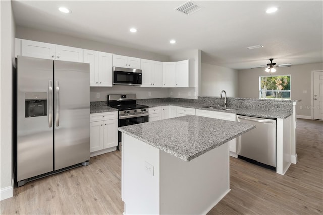 kitchen featuring white cabinets, a kitchen island, sink, stainless steel appliances, and light stone counters