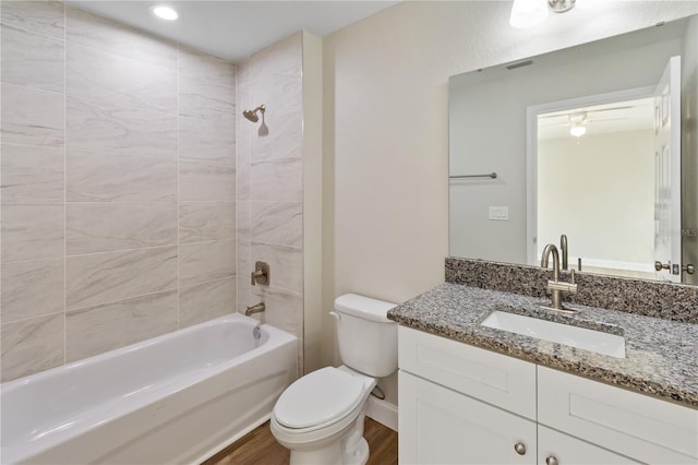 full bathroom featuring hardwood / wood-style floors, tiled shower / bath combo, vanity, and toilet