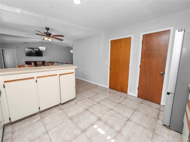 kitchen featuring a textured ceiling, ceiling fan, stainless steel fridge, and white cabinetry