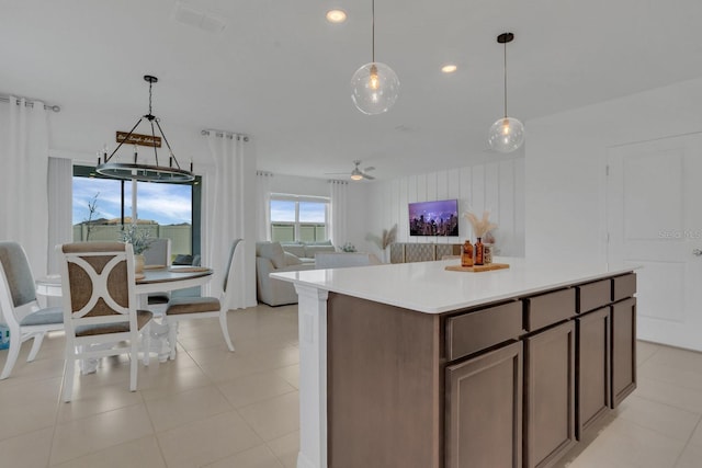 kitchen with a center island, dark brown cabinets, light tile patterned floors, pendant lighting, and ceiling fan