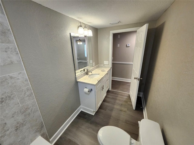 bathroom featuring vanity, wood finished floors, baseboards, toilet, and a textured wall