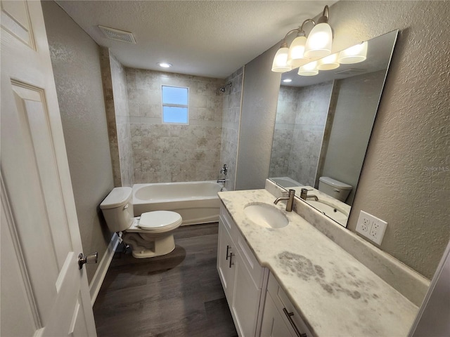 bathroom with visible vents, toilet, a textured ceiling, wood finished floors, and a textured wall