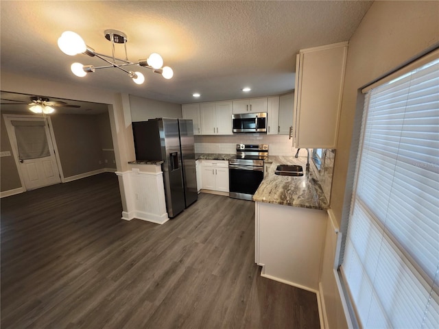 kitchen featuring dark wood-style floors, light stone countertops, a sink, stainless steel appliances, and white cabinetry