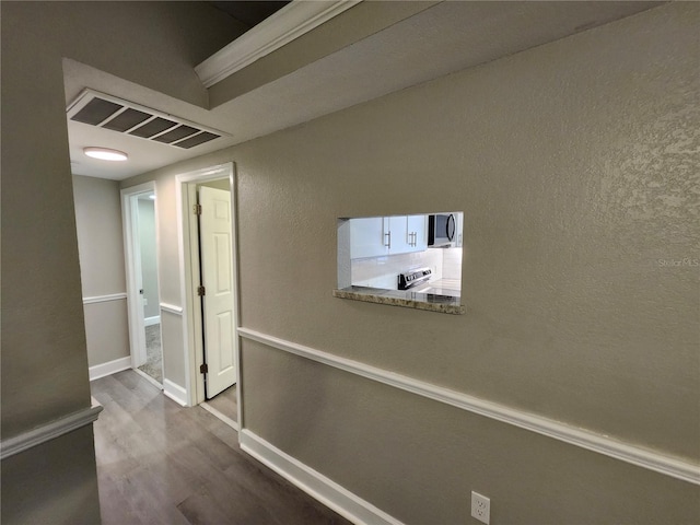 hall with dark wood finished floors, baseboards, visible vents, and a textured wall