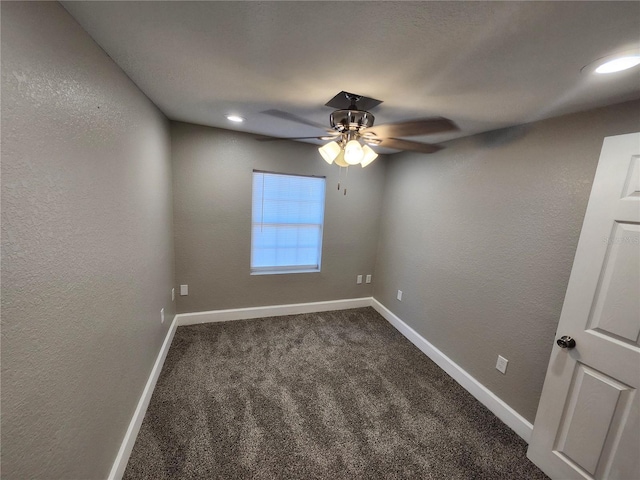 empty room featuring a textured wall, ceiling fan, baseboards, and dark colored carpet