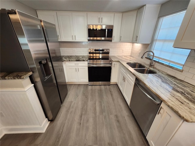 kitchen with a sink, light wood-style flooring, light stone counters, and stainless steel appliances