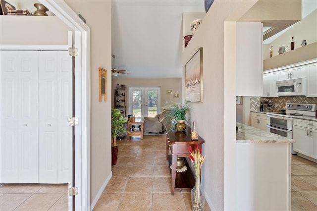 interior space with french doors, double oven range, light stone counters, white cabinets, and backsplash