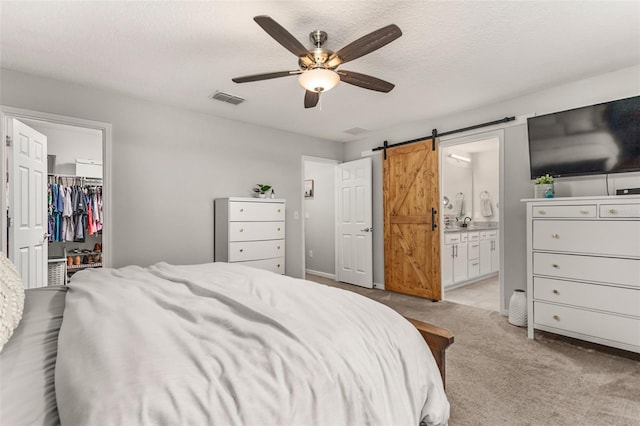 bedroom featuring a spacious closet, connected bathroom, ceiling fan, a closet, and a barn door