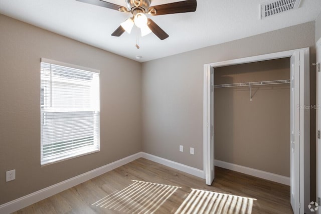 unfurnished bedroom with hardwood / wood-style floors, ceiling fan, a closet, and multiple windows