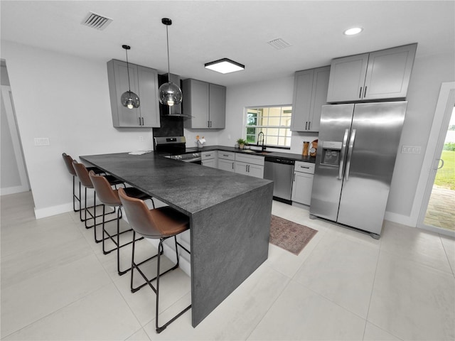 kitchen with kitchen peninsula, hanging light fixtures, stainless steel appliances, a kitchen bar, and gray cabinetry