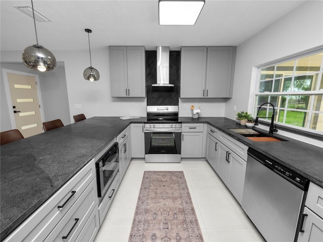 kitchen with a kitchen breakfast bar, gray cabinets, appliances with stainless steel finishes, sink, and wall chimney range hood