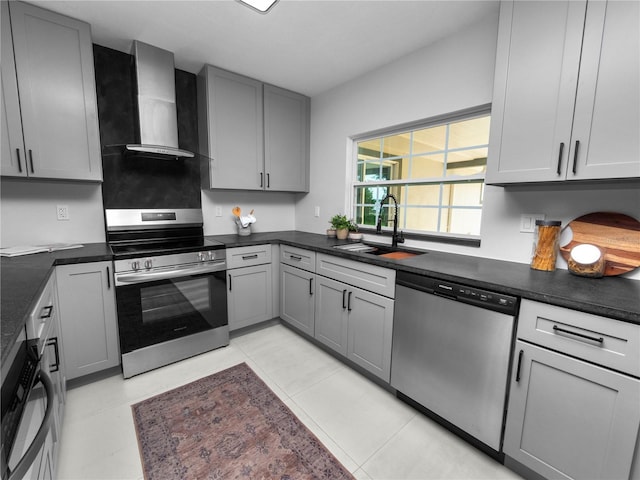 kitchen with stainless steel appliances, wall chimney range hood, gray cabinetry, and sink