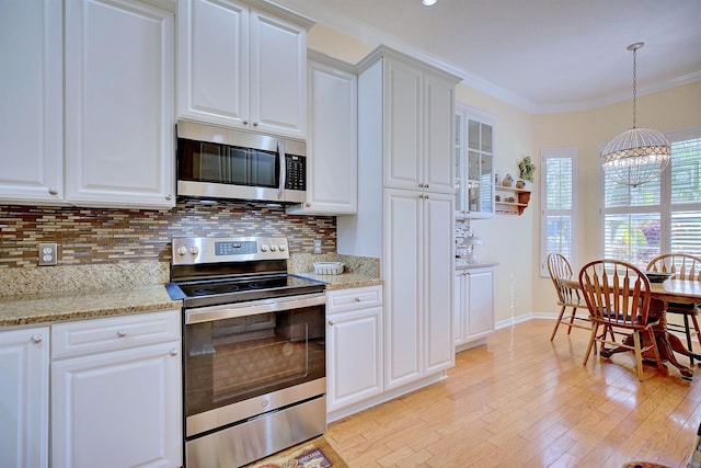 kitchen with stainless steel appliances, ornamental molding, white cabinets, and light stone countertops