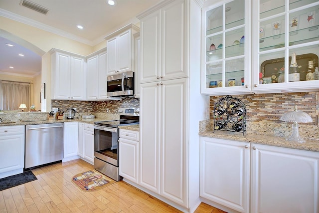 kitchen featuring light stone countertops, decorative backsplash, white cabinets, appliances with stainless steel finishes, and ornamental molding