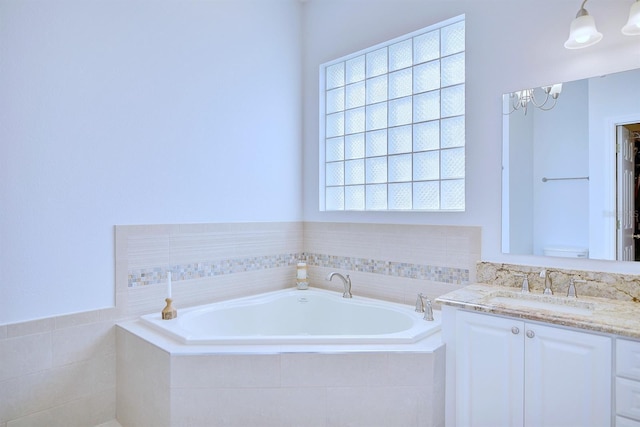 bathroom with a notable chandelier, tiled tub, and vanity