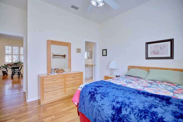 bedroom with ceiling fan, light wood-type flooring, ensuite bath, and a high ceiling