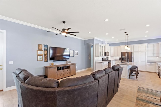 living room with crown molding, light wood-type flooring, sink, and ceiling fan