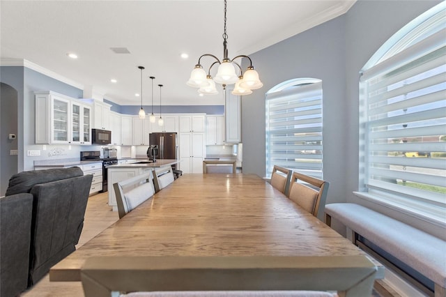 dining space featuring sink, a chandelier, a healthy amount of sunlight, and ornamental molding