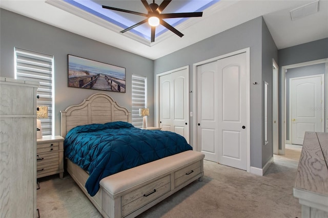 bedroom with ceiling fan, light colored carpet, and multiple closets