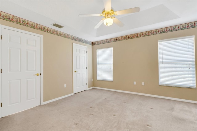 carpeted empty room with ceiling fan and a tray ceiling