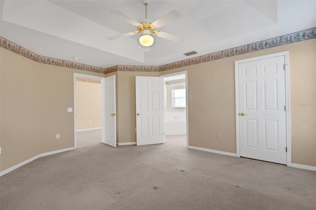 unfurnished bedroom with a raised ceiling, ceiling fan, and light colored carpet