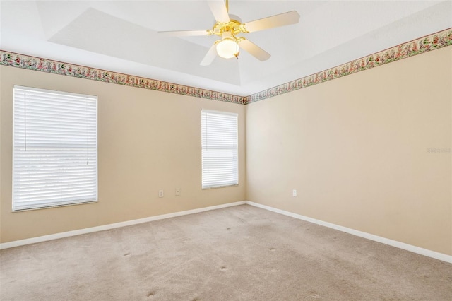 spare room featuring ceiling fan, light colored carpet, and a tray ceiling