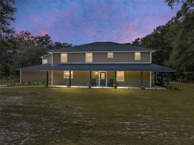 back house at dusk featuring covered porch and a yard