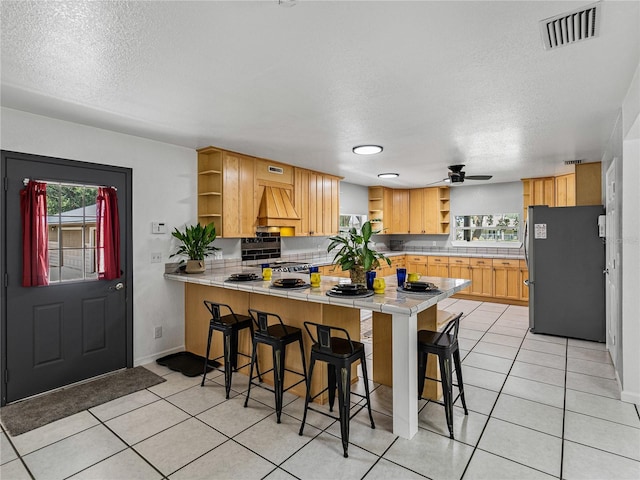 kitchen with ceiling fan, a kitchen bar, kitchen peninsula, and stainless steel refrigerator