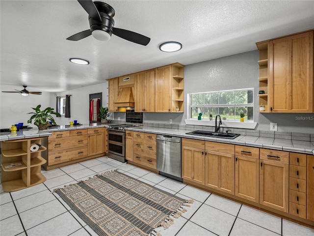 kitchen featuring custom exhaust hood, sink, light tile patterned flooring, stainless steel appliances, and tile counters