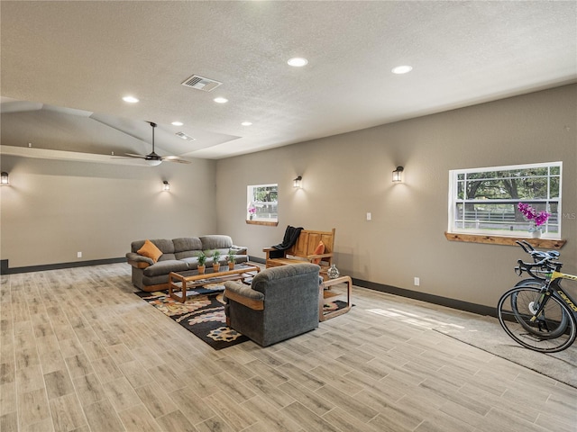 living room with ceiling fan, light wood-type flooring, vaulted ceiling, and a textured ceiling