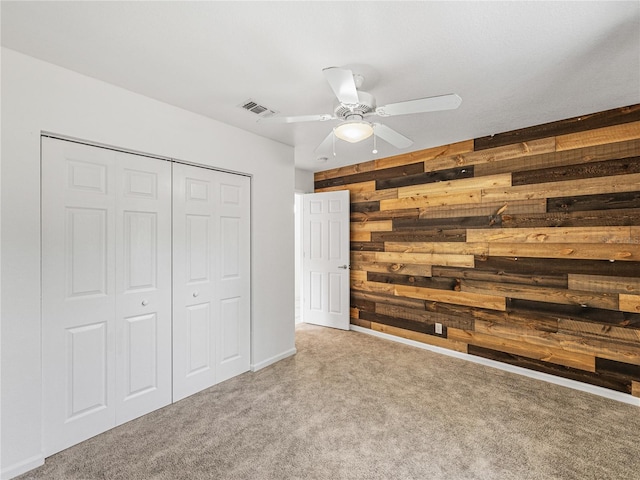 unfurnished bedroom with ceiling fan, a closet, carpet, and wooden walls