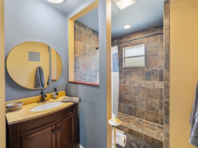 bathroom with a textured ceiling, tiled shower, and vanity