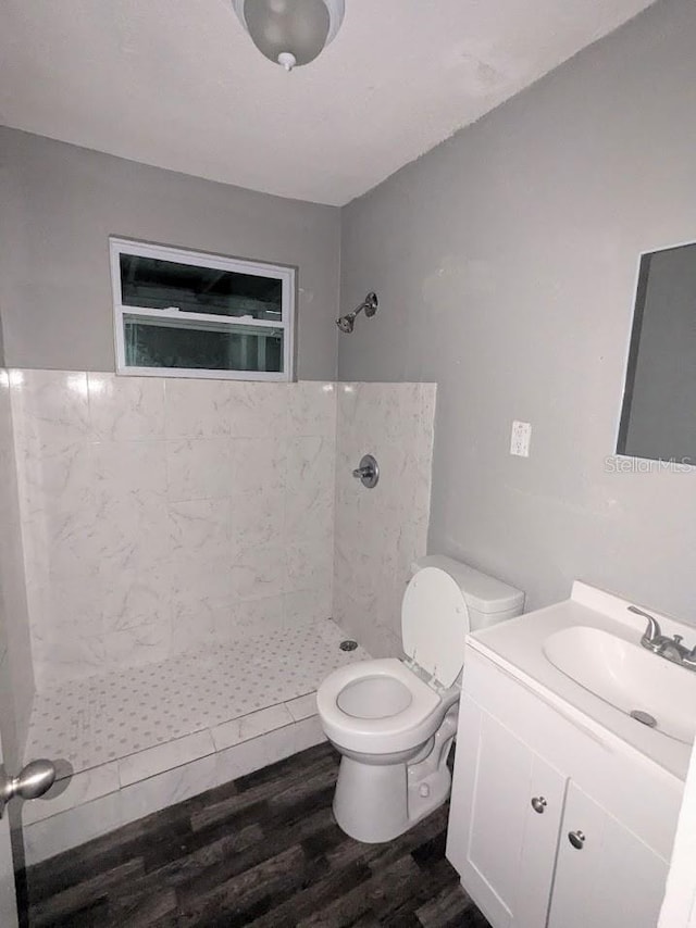 bathroom with toilet, a tile shower, wood-type flooring, and vanity