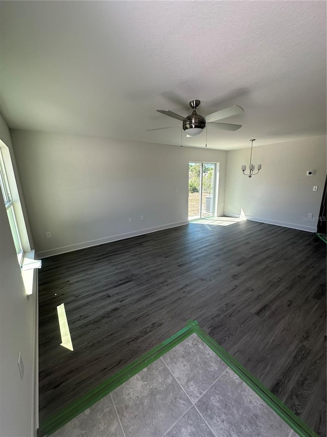 unfurnished living room with dark wood-style floors, a textured ceiling, ceiling fan with notable chandelier, and baseboards