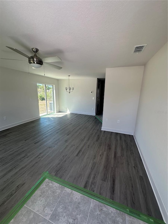 empty room featuring a textured ceiling, dark wood-type flooring, visible vents, and baseboards