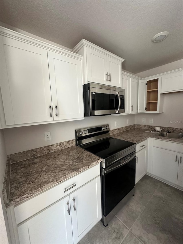 kitchen with stainless steel appliances, dark countertops, white cabinetry, a sink, and a textured ceiling