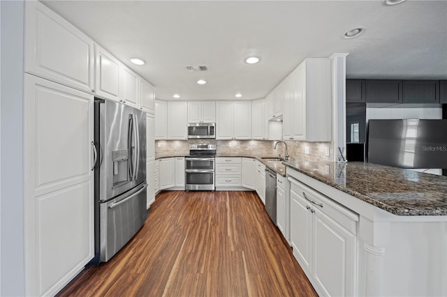 kitchen featuring stainless steel appliances, white cabinetry, dark stone counters, and sink