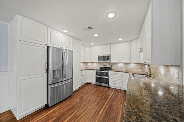 kitchen with appliances with stainless steel finishes, dark stone countertops, and white cabinetry