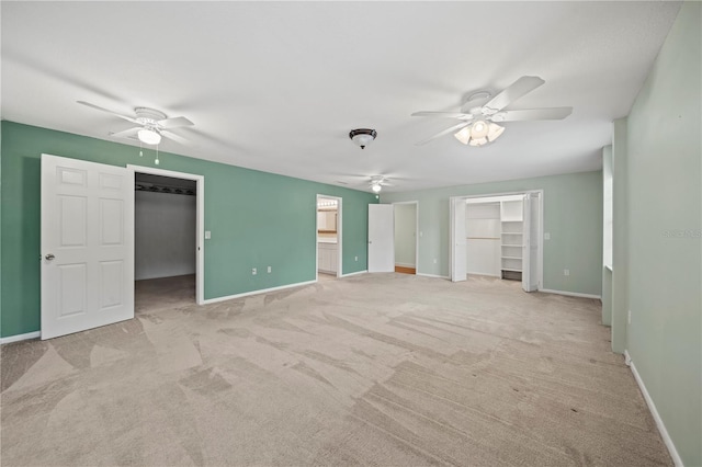 unfurnished bedroom with ceiling fan, a walk in closet, light carpet, and connected bathroom